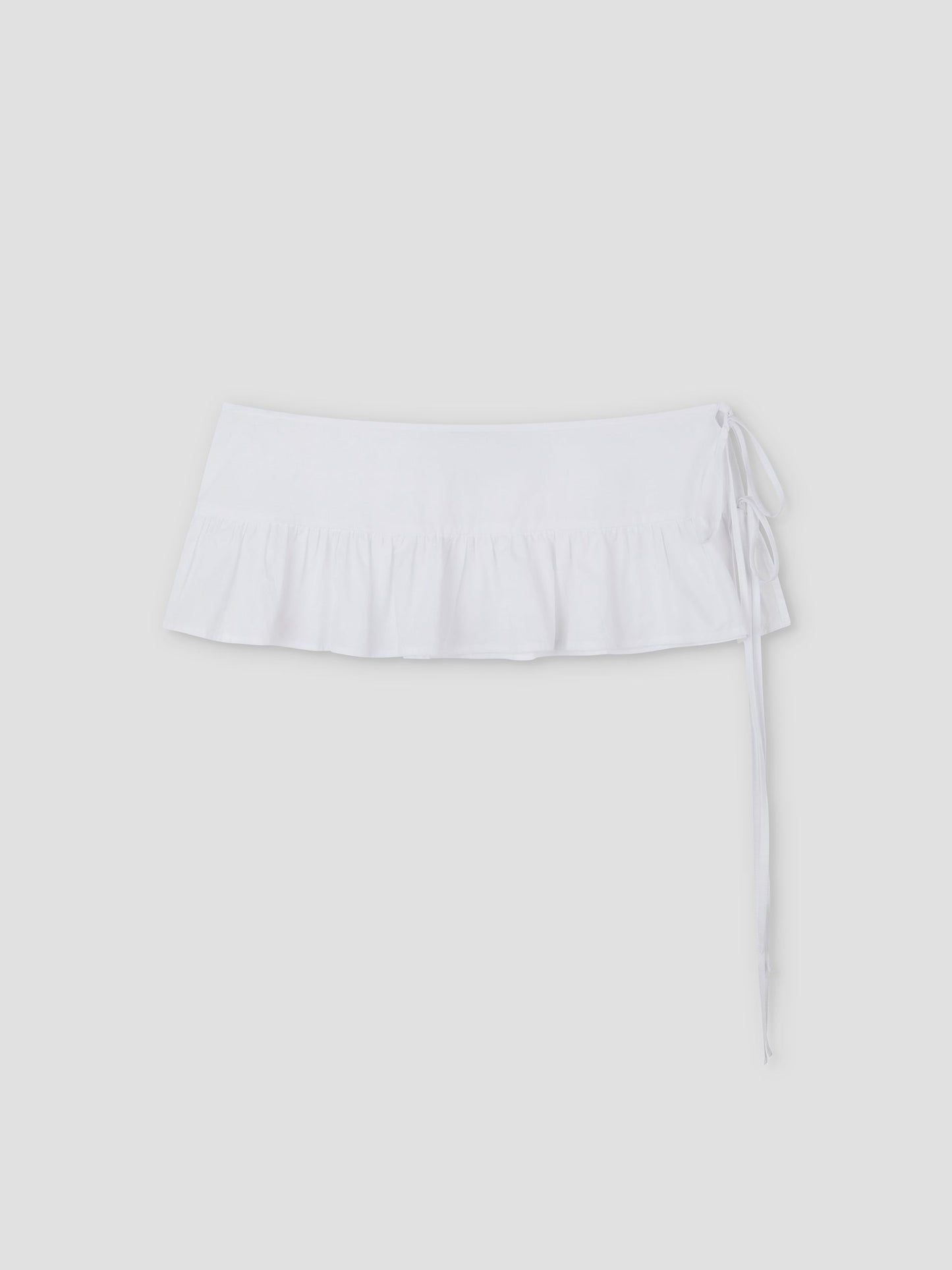 The Flounce Belt is a white mini skirt featuring a ruffled hem and side tie, shown against a plain light gray background.