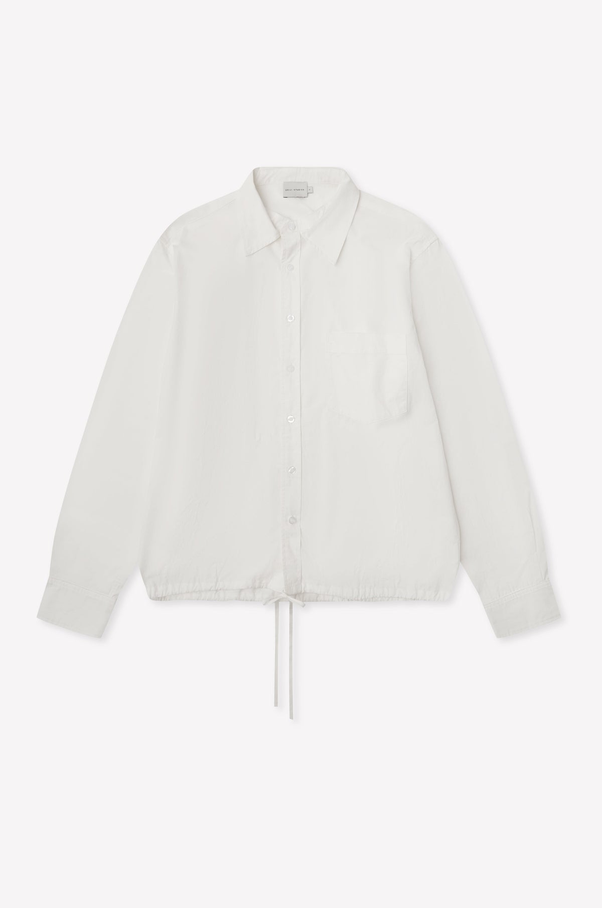 The Stand Shirt - White is a long-sleeved, oversized cotton shirt featuring a single chest pocket, mandarin collar, and drawstring hem, shown on a white background.