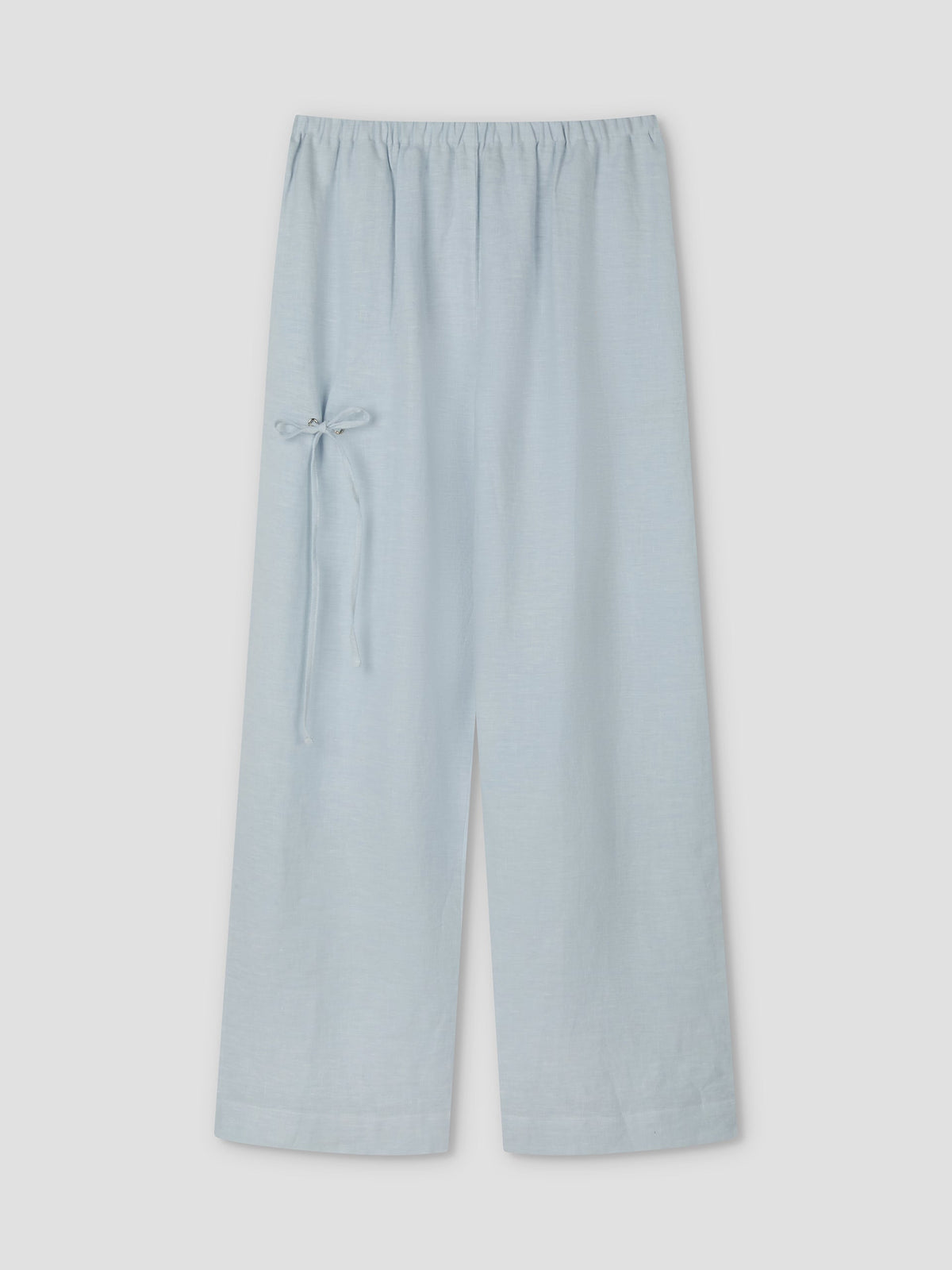 The Eyelet Pant - Soft Blue by Deiji Studios features wide-leg linen, a relaxed ankle length, an elastic waistband, and a small bow tie detail on the left side, displayed against a plain light background.