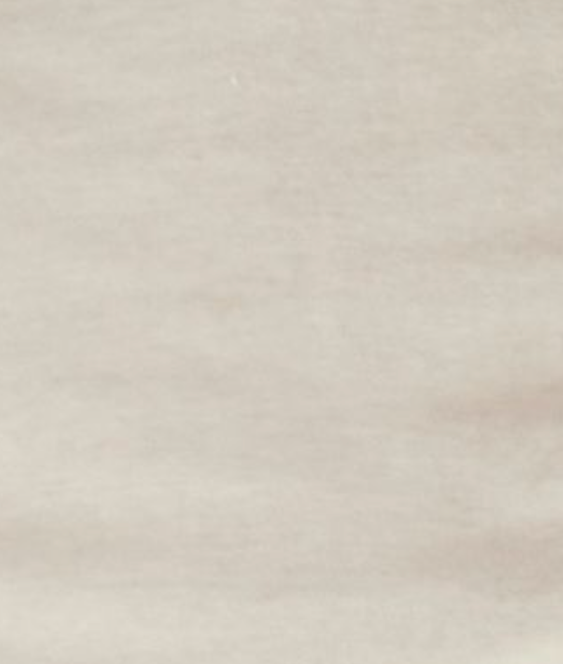A close-up of the Flounce Tee - Cream reveals a smooth, light beige surface with subtle, natural variations and delicate lines, echoing minimalist style and the refined texture of a fitted tee.