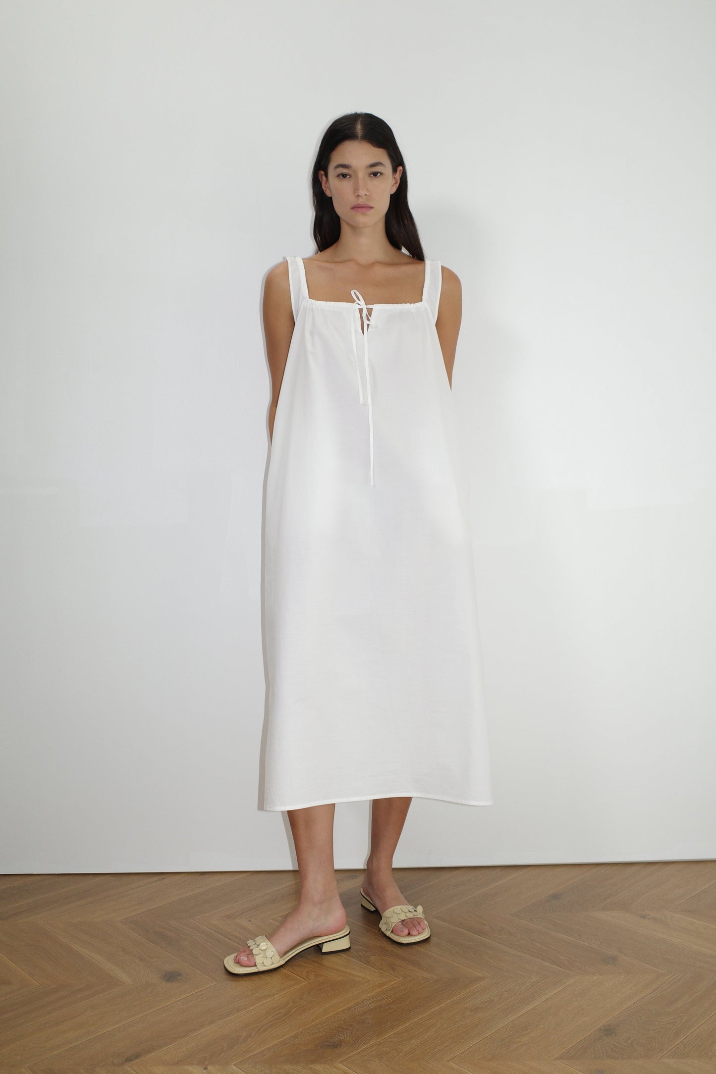 female model wears the paper dress by Deiji Studios in white, a crisp and lightweight maxi-length dress features a flattering gathered square neckline with keyhole and tie front feature and side seam pockets, made from GOTS certified organic cotton poplin