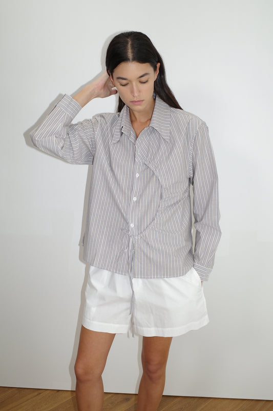 female model wears the arch tie shirt by Deiji Studios in seas stripe


a classic crisp button up shirt in a boxy fit, featuring a dropped back yoke, dropped shoulders, a classic shirting cuff with a layered arch fabric detail on front with tie


made from 100% GOTS certified organic cotton poplin

paired with a white cotton short