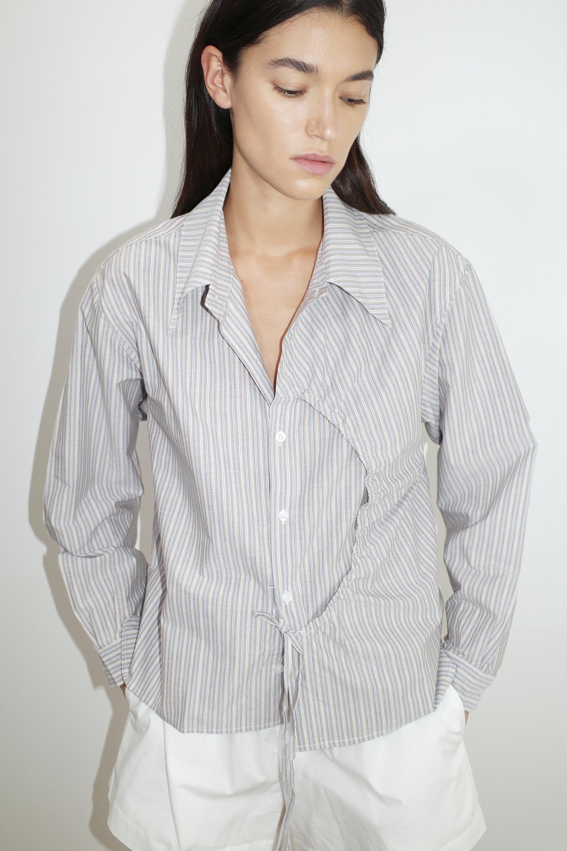 female model wears the arch tie shirt by Deiji Studios in seas stripe


a classic crisp button up shirt in a boxy fit, featuring a dropped back yoke, dropped shoulders, a classic shirting cuff with a layered arch fabric detail on front with tie


made from 100% GOTS certified organic cotton poplin

paired with a white cotton short