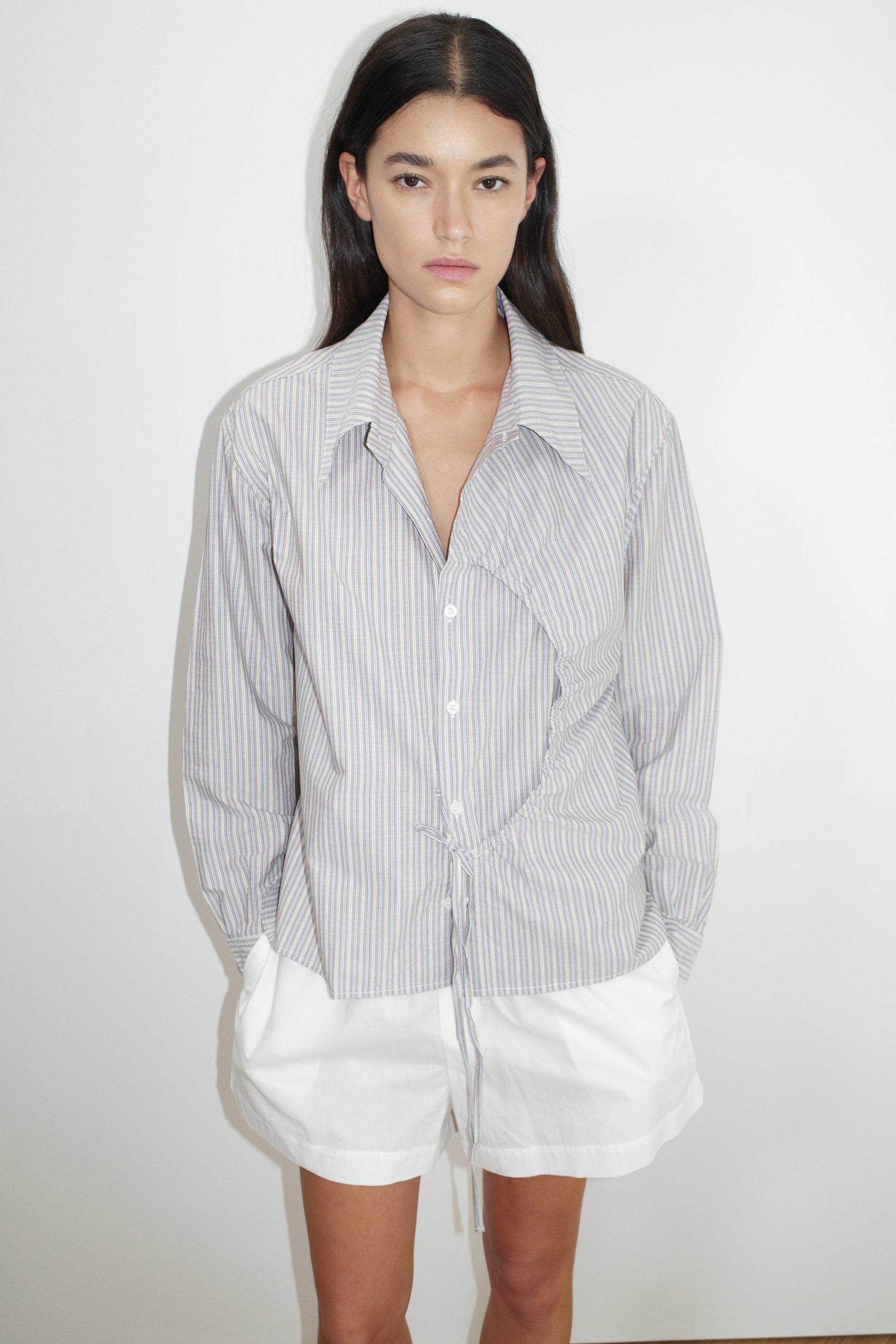 female model wears the arch tie shirt by Deiji Studios in seas stripe


a classic crisp button up shirt in a boxy fit, featuring a dropped back yoke, dropped shoulders, a classic shirting cuff with a layered arch fabric detail on front with tie


made from 100% GOTS certified organic cotton poplin

paired with a white cotton short