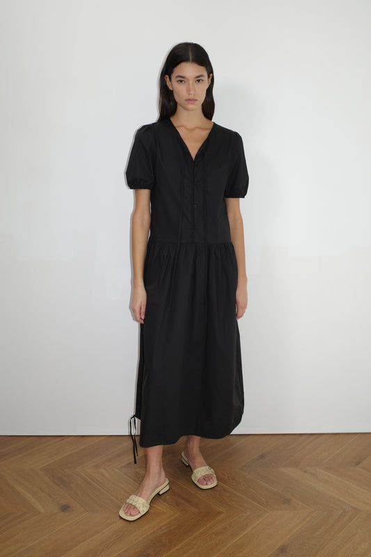 female model wears the draw hem dress by Deiji Studios in black


elevated everyday dress in mid length features a flattering v neckline with tie, button front detail with a drop waist, and soft elastic blouson sleeve


made from 100% organic cotton poplin