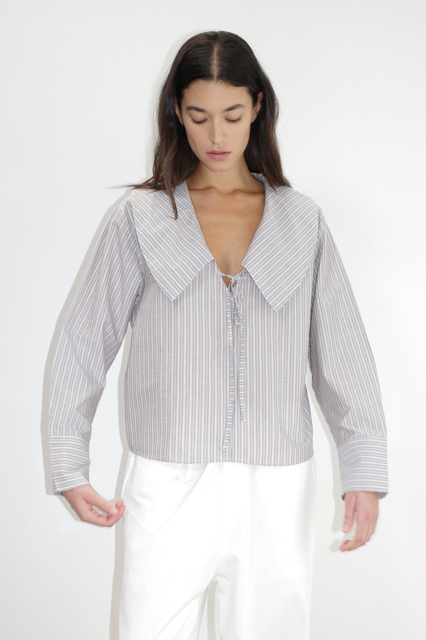 female model wears the collared tie shirt by Deiji Studios in seas stripe


a structured shirt features an oversized collar and cuff, tie at front collar opening, dropped shoulder and elongated sleeves in a boxy fit


made from 100% GOTS certified organic cotton poplin

paired with a white cotton trouser