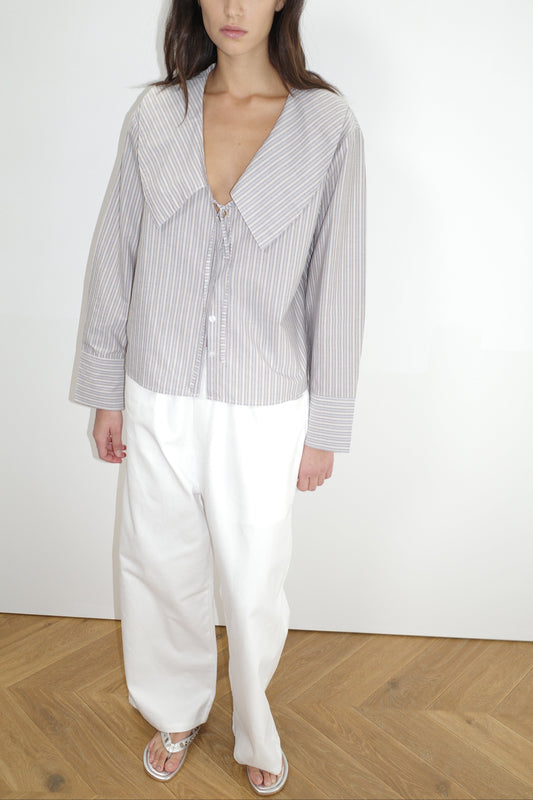 female model wears the collared tie shirt by Deiji Studios in seas stripe


a structured shirt features an oversized collar and cuff, tie at front collar opening, dropped shoulder and elongated sleeves in a boxy fit


made from 100% GOTS certified organic cotton poplin

paired with a white cotton trouser