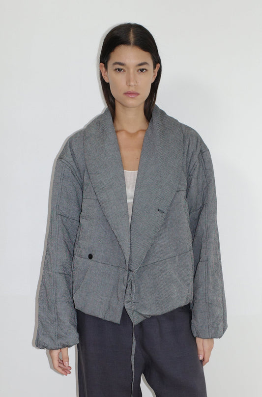 A woman with straight dark hair models the Exclusive Bubble Coat - Black White Stripe by 0, layering it over a light top and dark pants while standing against a plain white background.