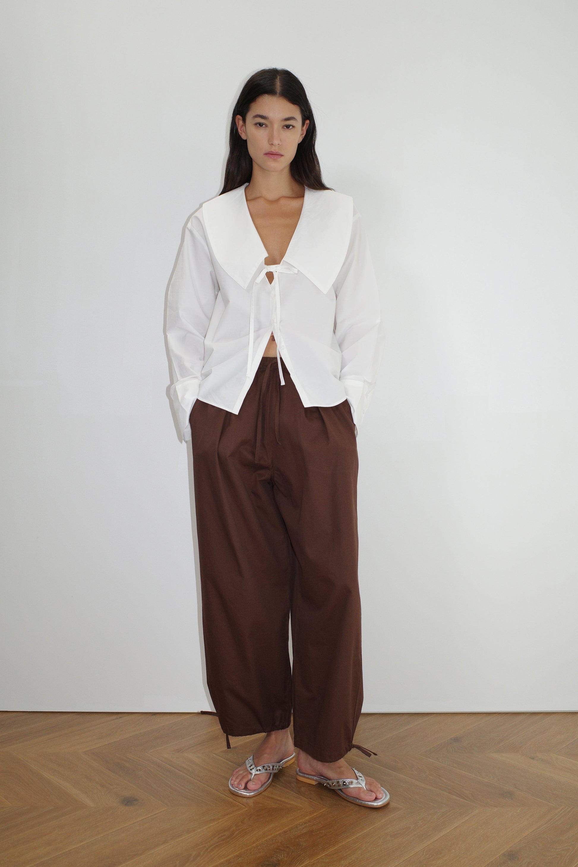 female model wears the collared tie shirt by Deiji Studios in white


a structured shirt features an oversized collar and cuff, tie at front collar opening, dropped shoulder and elongated sleeves in a boxy fit


made from 100% GOTS certified organic cotton poplin

paired with a brown cotton trouser