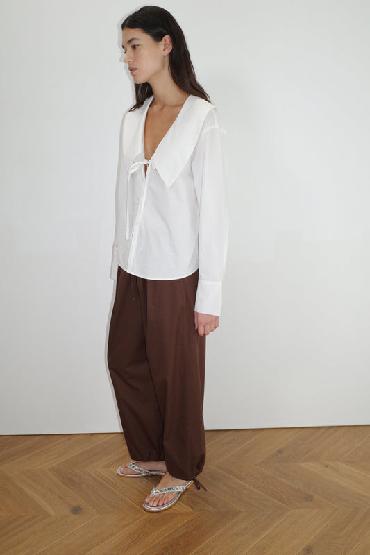 female model wears the collared tie shirt by Deiji Studios in white


a structured shirt features an oversized collar and cuff, tie at front collar opening, dropped shoulder and elongated sleeves in a boxy fit


made from 100% GOTS certified organic cotton poplin

paired with a brown cotton trouser