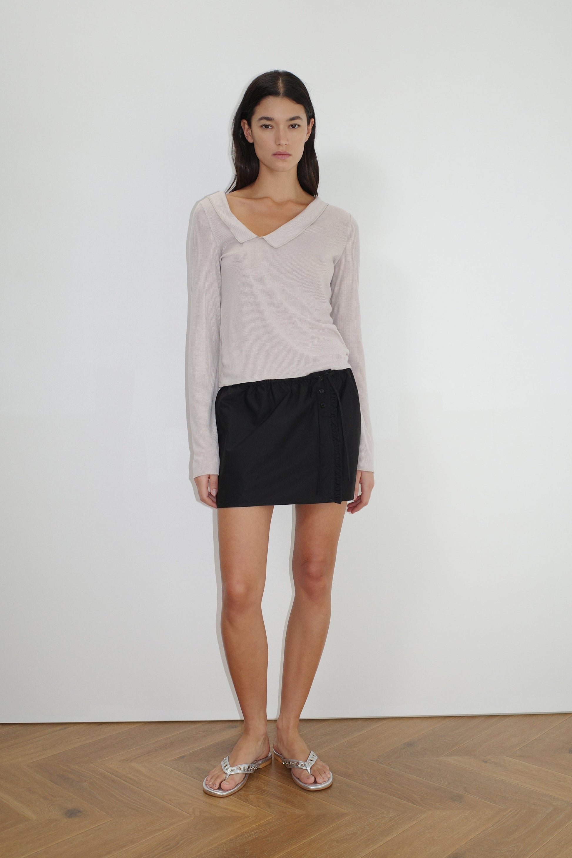 female model wears the ruffle mini skirt by Deiji Studios in black


simple mini skirt designed to sit at low waist features adjustable tie and ruffle edge on side with button detail


made from 100% GOTS certified organic cotton poplin

paired with a sheer knit long sleeve in beige