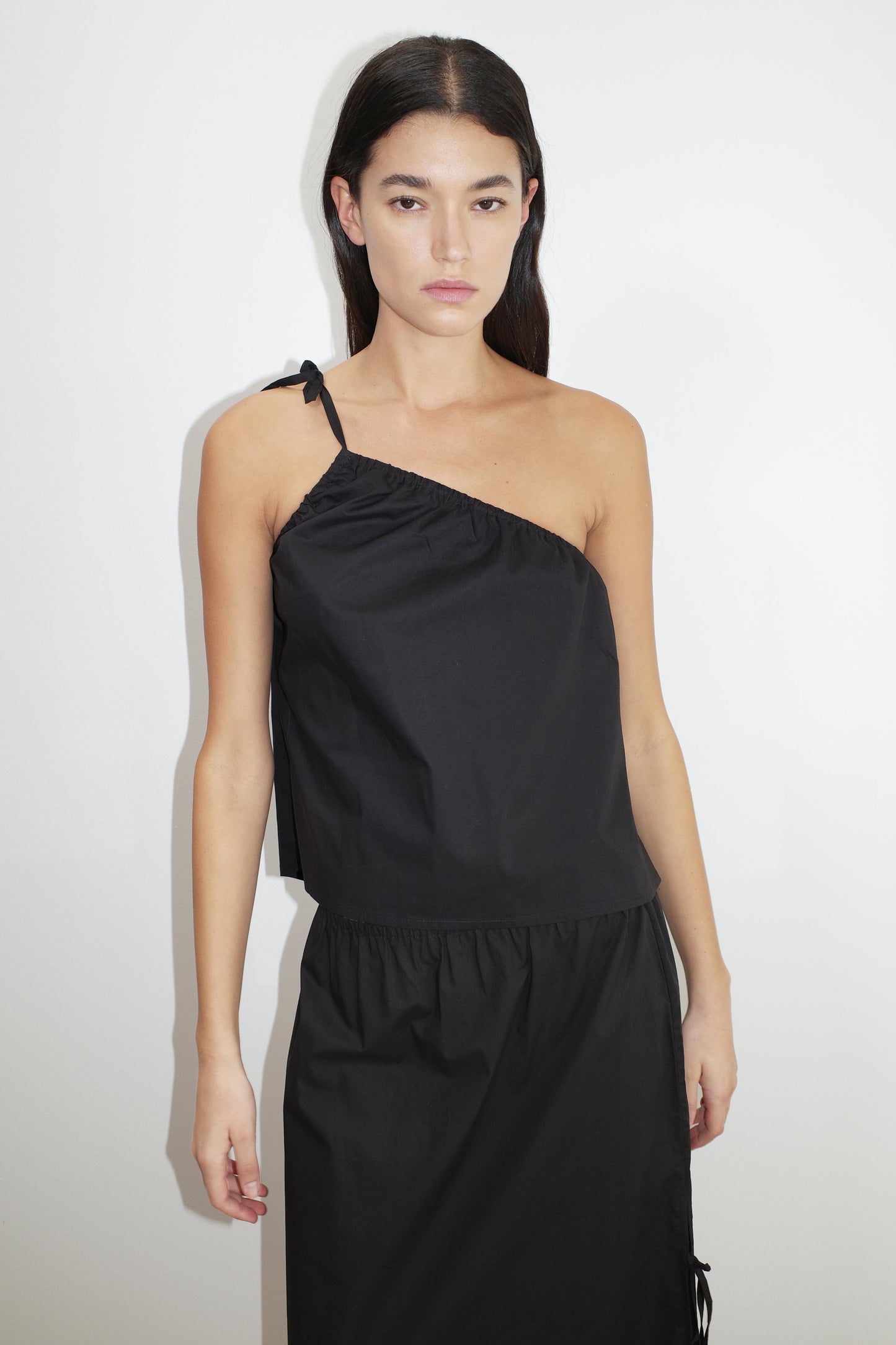 female model wears the ruched strap top by Deiji Studios in black


a lightweight one shoulder top featuring fine tie shoulder strap, fixed gathering on armholes and elasticated neckline for a relaxed fit


made from 100% organic cotton poplin

paired with a black skirt