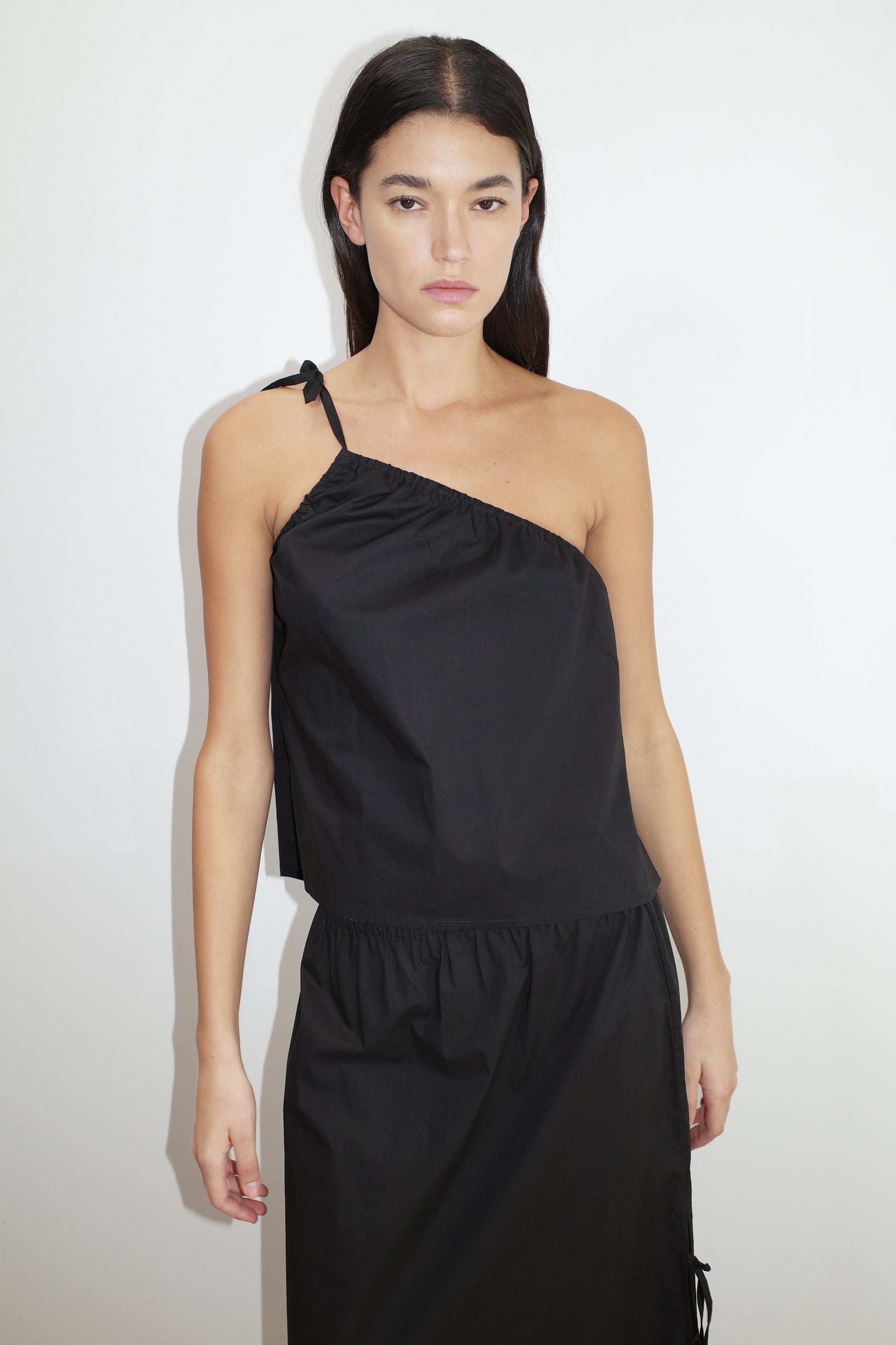 female model wears the ruched strap top by Deiji Studios in black


a lightweight one shoulder top featuring fine tie shoulder strap, fixed gathering on armholes and elasticated neckline for a relaxed fit


made from 100% organic cotton poplin

paired with a black skirt