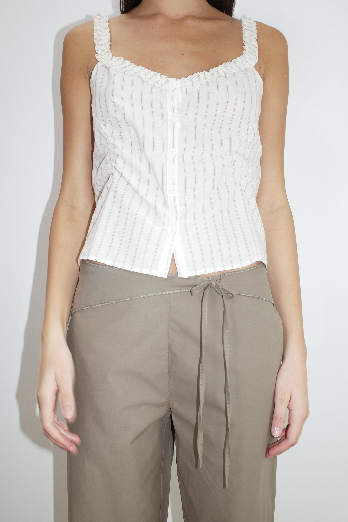female model wears the ruffle button top by Deiji Studios in raquette stripe


a button up top featuring a butter base with mixed blue stripe, flattering v neckline, self-fabric ruffles along the straps and designed elasticated gatherings


made from 100% GOTS organic cotton

paired with a clay green pant