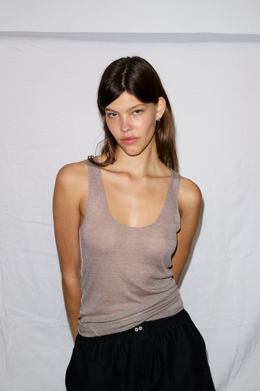 A young woman with straight brown hair stands against a plain white background, wearing the Knit Tank in light brown and black pants, looking slightly to the side with a neutral expression.
