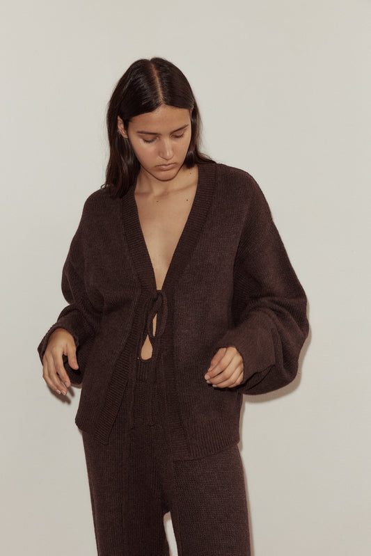 Close up shot of model wearing the Two Tie Cardigan in Plum by Deiji Studios, styled with the Straight Leg Knit Pant in Plum. Cardigan features v neckline with two long knit ties at front, one at bust and one at waist.