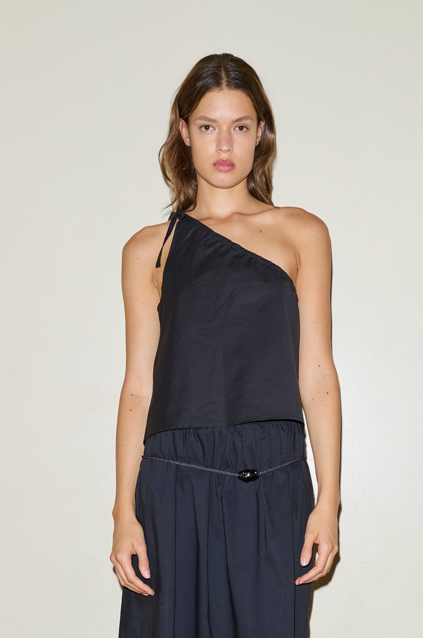 A woman with straight brown hair wears the black Multi Strap Top and a matching black skirt, standing against a plain light background and looking directly at the camera with a neutral expression.