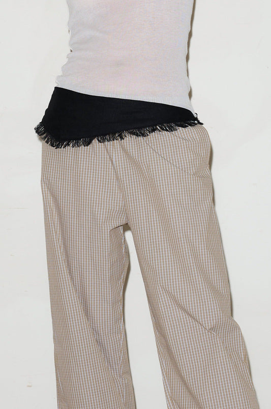 A person stands against a plain white background wearing beige checkered pants, a white ribbed sleeveless top, and the Linen Fray belt in Black tied around their waist.