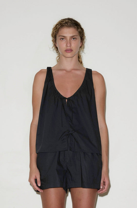 A woman with curly hair wears the Cotton Bind Top - Black by Deiji Studios and matching shorts, standing against a plain white background and looking directly at the camera with a neutral expression.