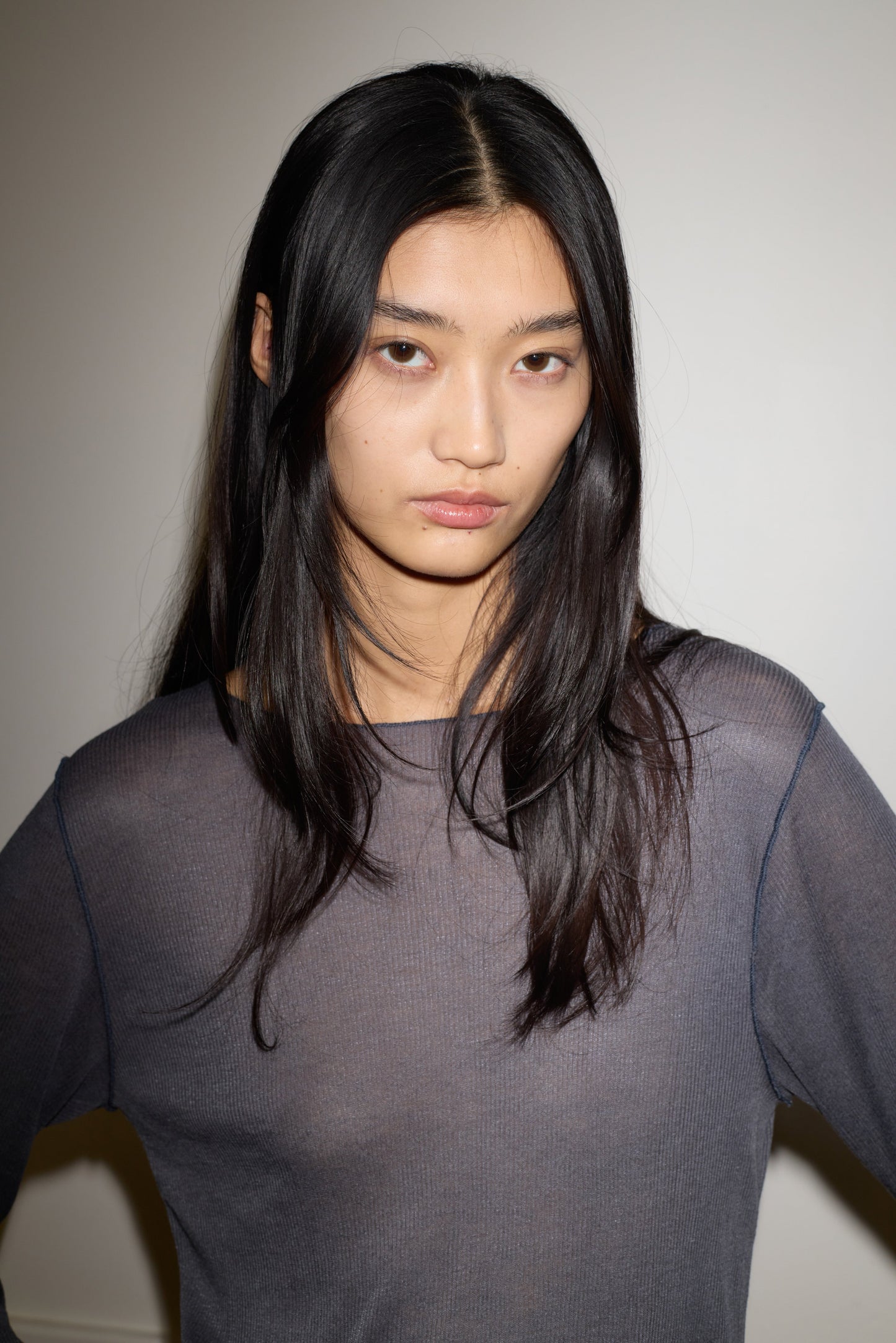 A young woman with long, straight black hair and a neutral expression stands against a plain white background, wearing the Knit Long Sleeve - Steel by 0.