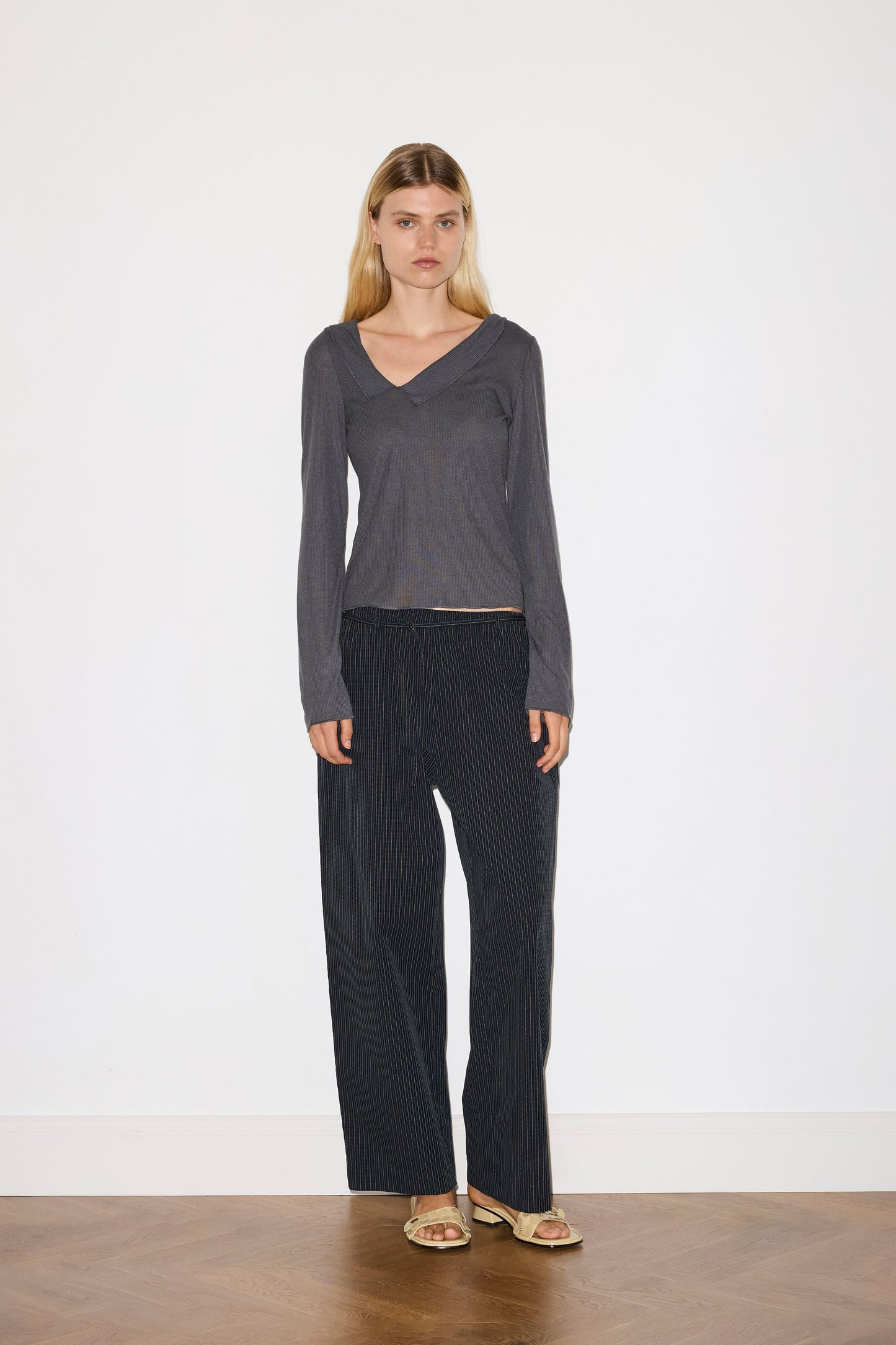 blonde female model wears grey long sleeve top, worn with a navy and yellow striped trouser 