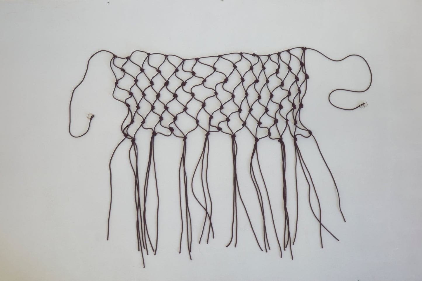 A handwoven black macramé belt made from recycled polyester, featuring loose ends and fringes, displayed flat on a white background.