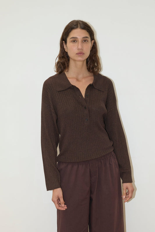 A woman with wavy brown hair wears the Polo Knit - Dark Almond, a long-sleeve collared top with loose brown pants, standing against a plain white background.