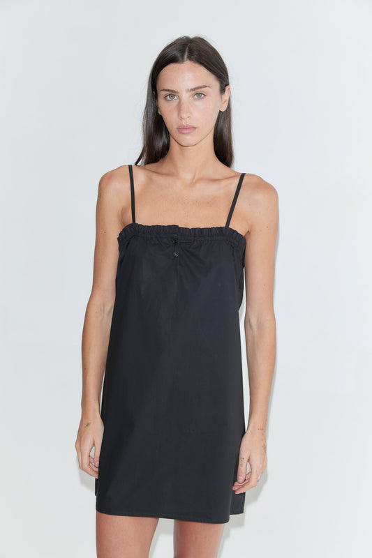 A cropped front view of the Frill Placket Dress - Black by Deiji Studios, a black mini dress with thin straps and a gathered, buttoned frill placket at the neckline, against a plain white background.