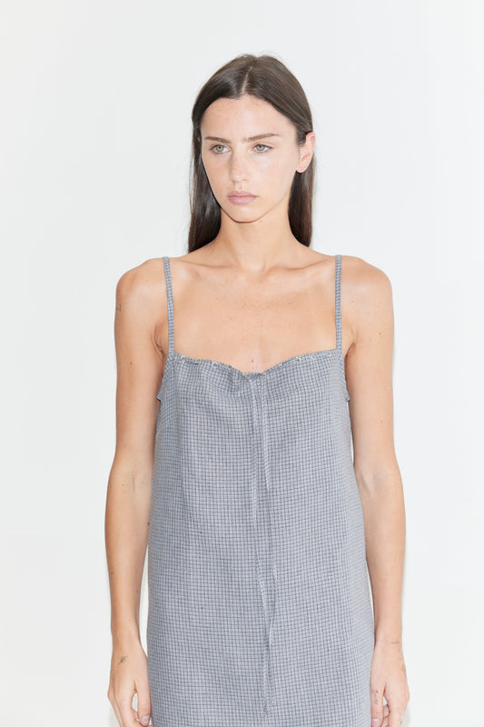 A cropped view of the Weave Mini - Indigo Check by Deiji Studios, an indigo micro-check linen mini dress with thin straps, a gathered bust and drawstring front tie, against a plain white background.