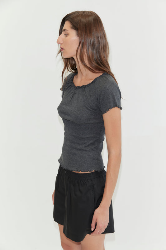 A woman with long brown hair stands in profile against a white background, wearing a fitted gray short-sleeve top and black Organic Cotton Boxer shorts with an elastic waist.