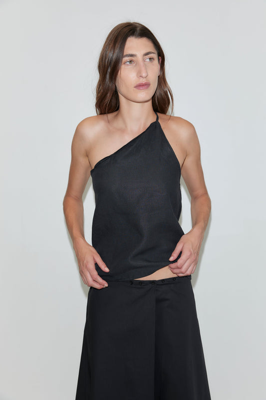 A person with long brown hair wears a black Deiji Studios wrap skirt, standing against a plain light-colored background.