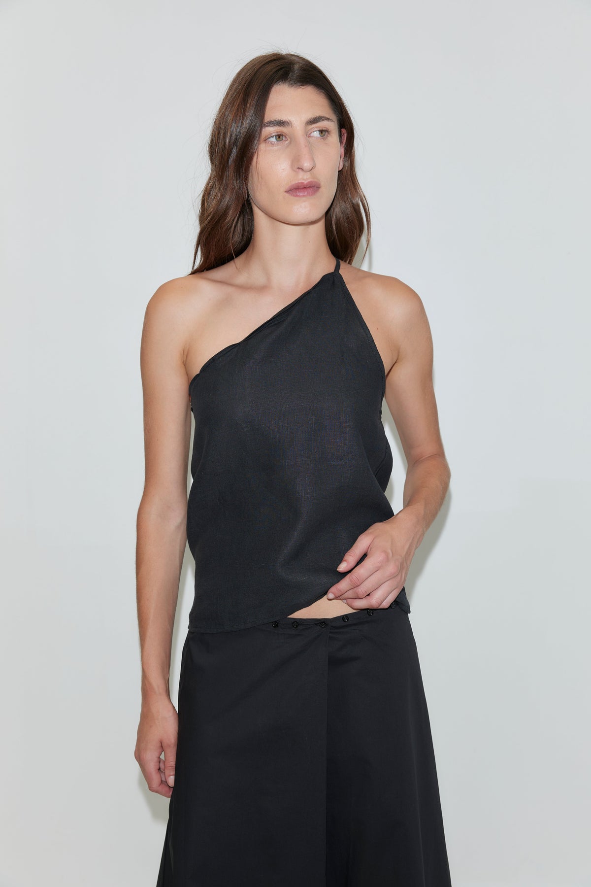 A person with long brown hair wears the Half Halter - Black from Deiji Studios and black pants, standing against a plain white background.