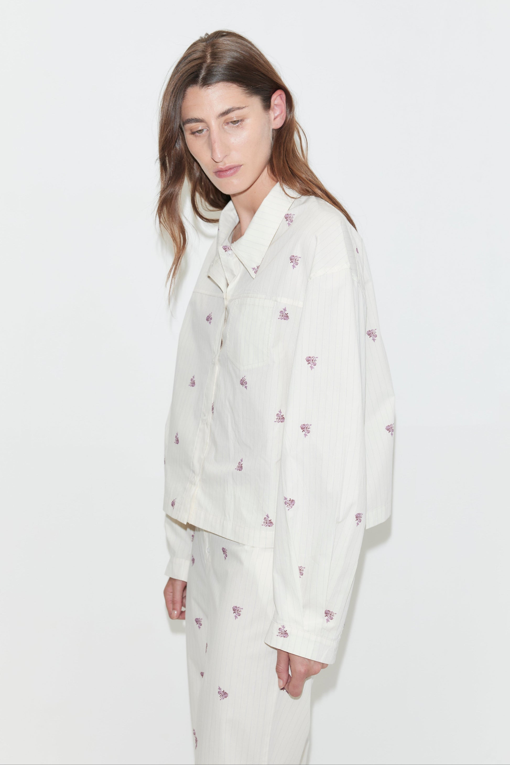 A person with long brown hair wears the oversized cotton poplin Boxy Long Set - Floral Stripe, which features a subtle purple floral pattern, standing against a plain white background.