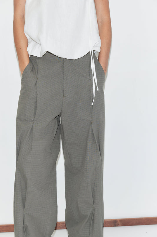 A cropped view of the Multi Pleat Pant - Moss Stripe by Deiji Studios, moss-green fine-check wide-leg pleated trousers with side pockets, worn with a white top against a plain white background.