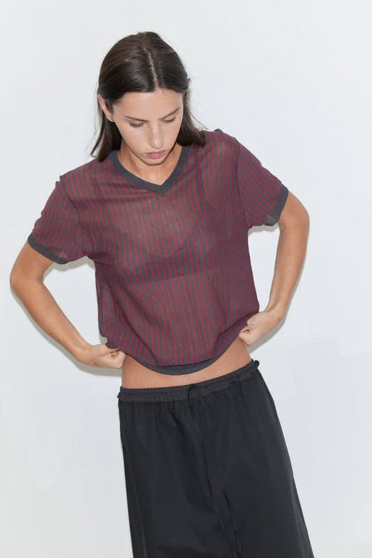 A cropped view of a woman wearing the One Frill Skirt - Black by Deiji Studios, a black skirt with a drawcord waist, and a red striped knit tee, against a plain white background.