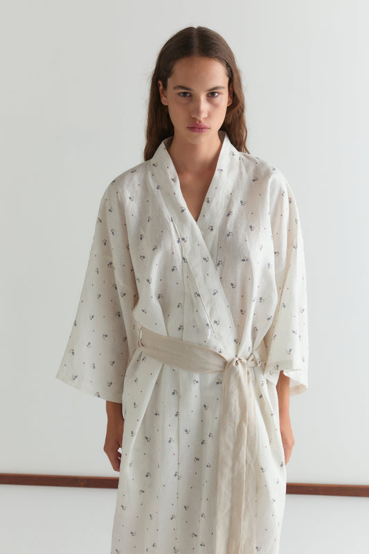 A woman with long brown hair models the 02 robe - vintage floral, which features a linen waist tie, standing against a plain white background.