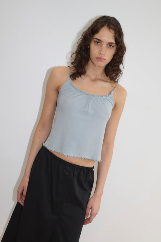 Model wearing the Cotton Flounce Tank - Baby Blue, featuring a ruffled neckline and lettuce hem, paired with a black wide-leg maxi skirt against a white background.