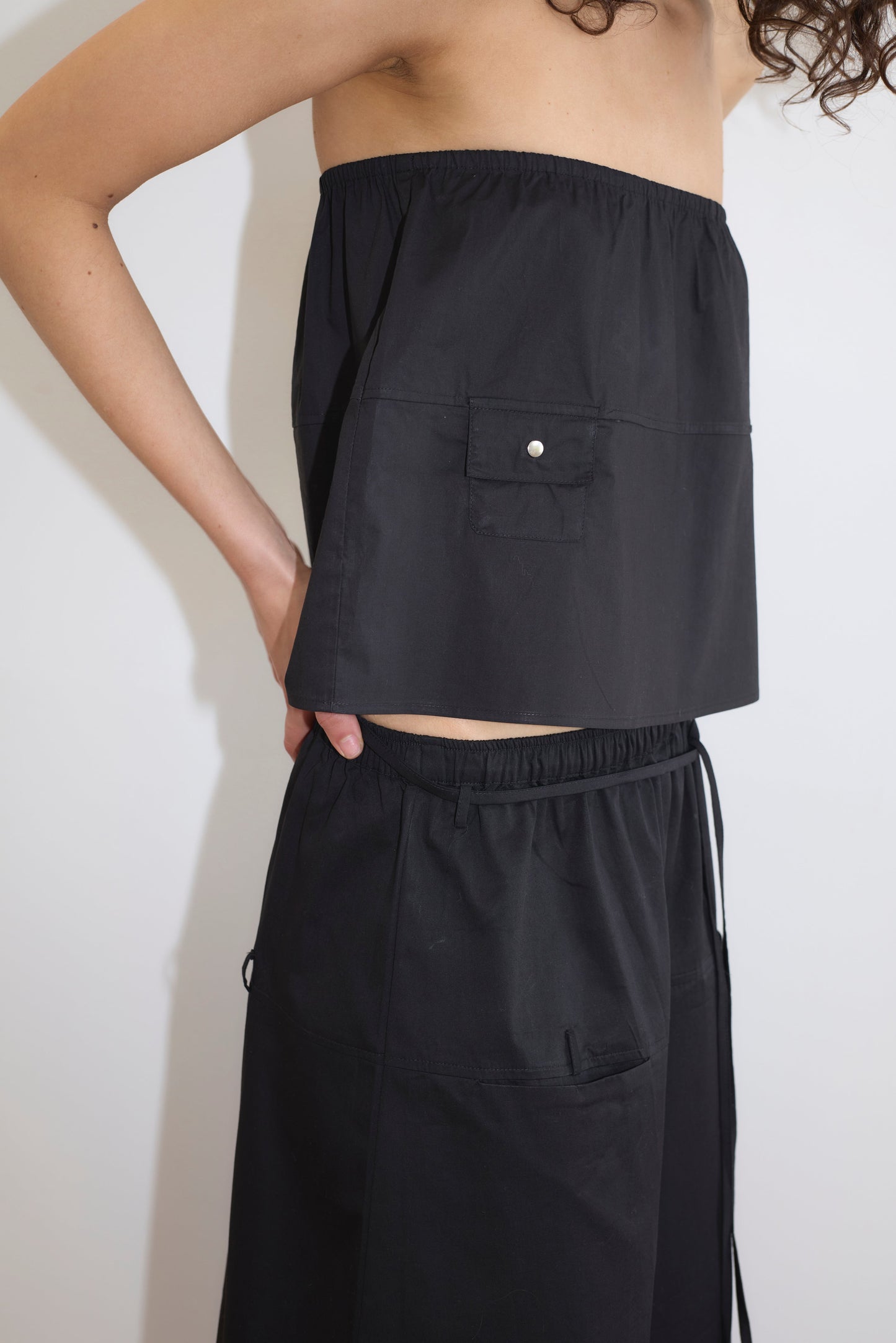 A person models the Pocket Skirt - Black, a strapless, loose-fitting skirt with a front pocket, against a white background. Only the upper body and part of the lower body are visible.