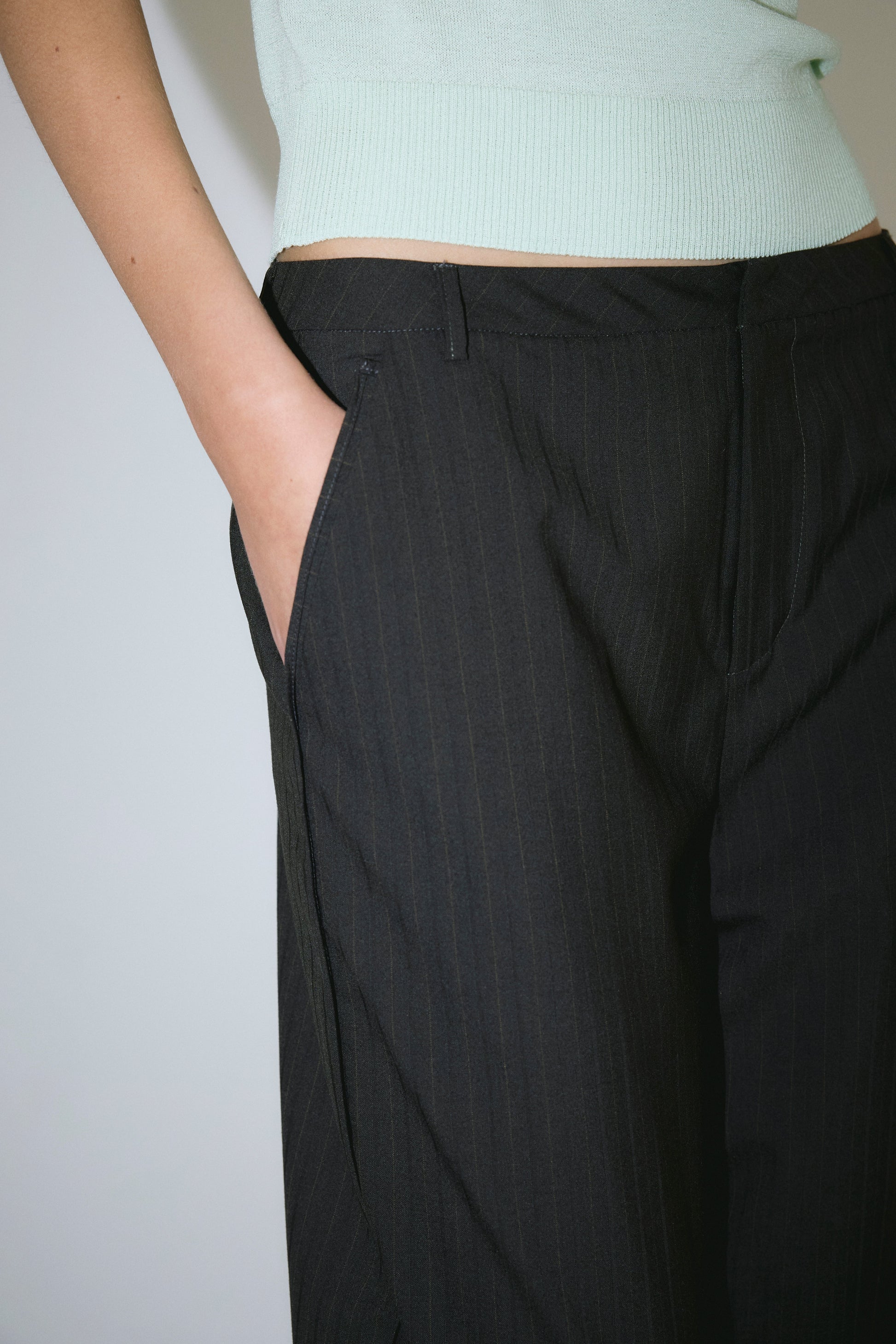 A person wearing the Bind Pant - Charred Black Stripe with their right hand in the pocket and a light mint green sleeveless top. Only the torso and upper legs are visible.