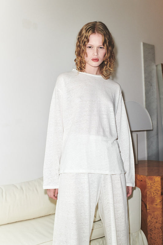 A person with wavy blonde hair stands indoors, wearing the Soft Long Sleeve Top and matching wide-leg pants. They are in front of a white couch and a wooden side table with a lamp.