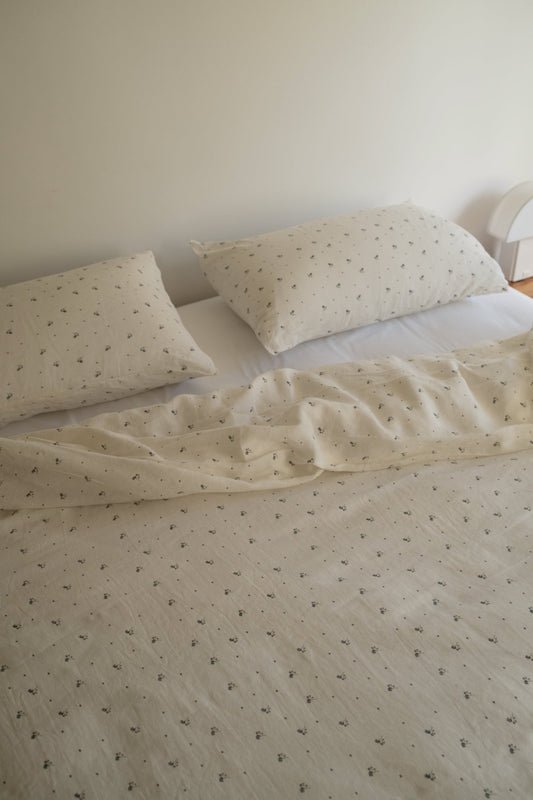 A neatly made bed features Deiji Studios’ Duvet cover - vintage floral with white sheets and pillowcases, all with a small, delicate pattern, set against a plain light-colored wall.