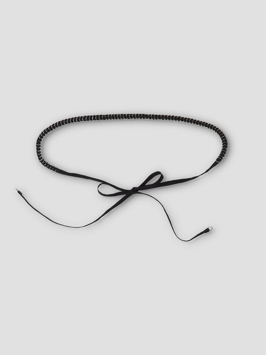 The Ring Loop Belt is a thin black belt with white stitching, tied in a bow at the center, featuring long loose ends, shown on a plain light background.