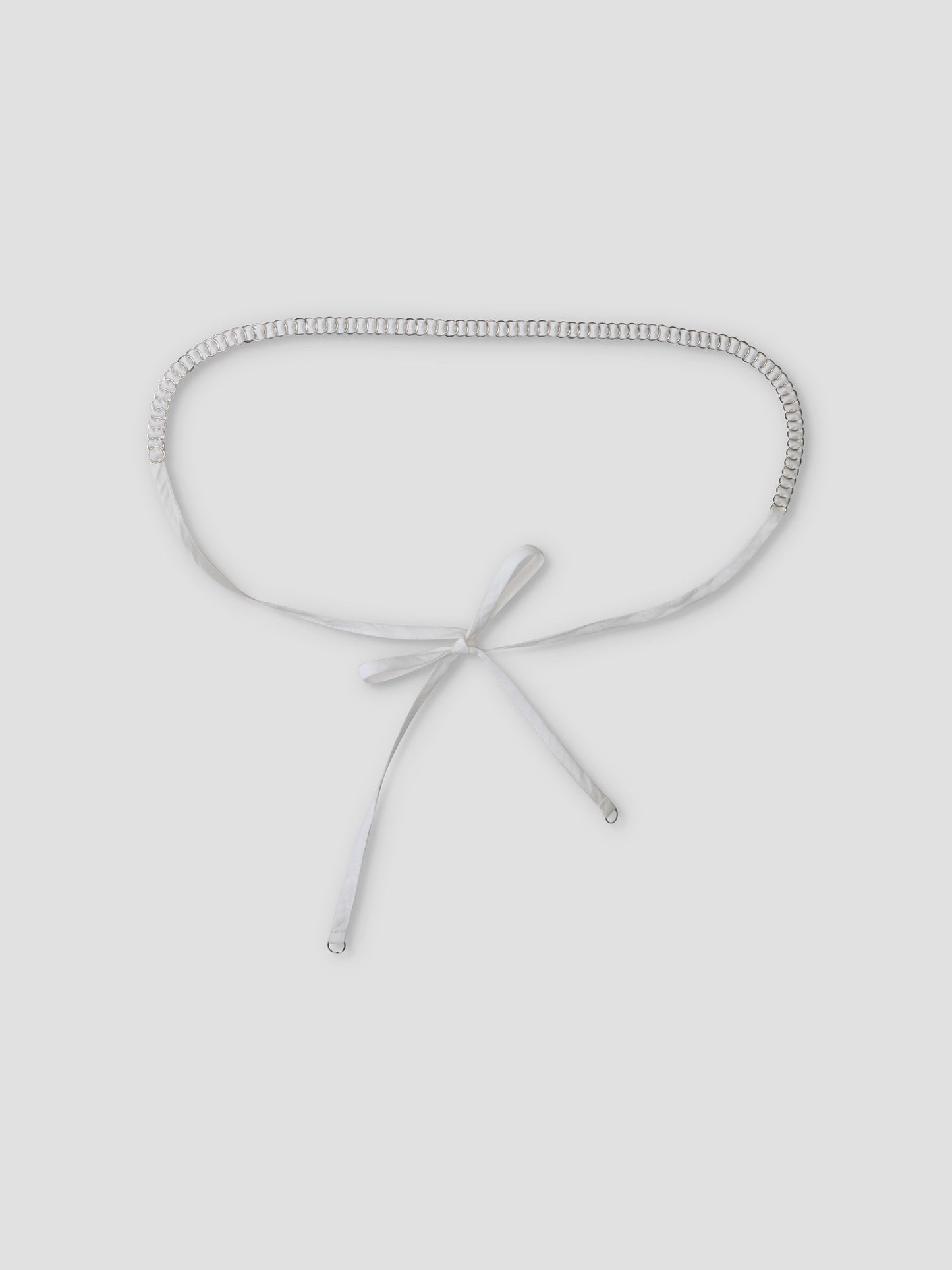 The Ring Loop Belt, featuring a silver chain and white ribbon tie closure, is shown flat on a light grey background.