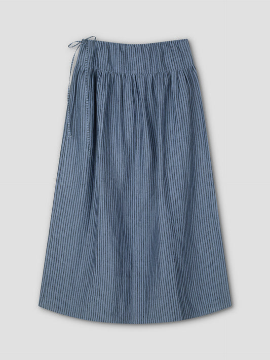 The Maxi Skirt - Azure Stripe is a knee-length, blue and white striped skirt featuring a gathered waist and left-side tie, shown on a plain light grey background.