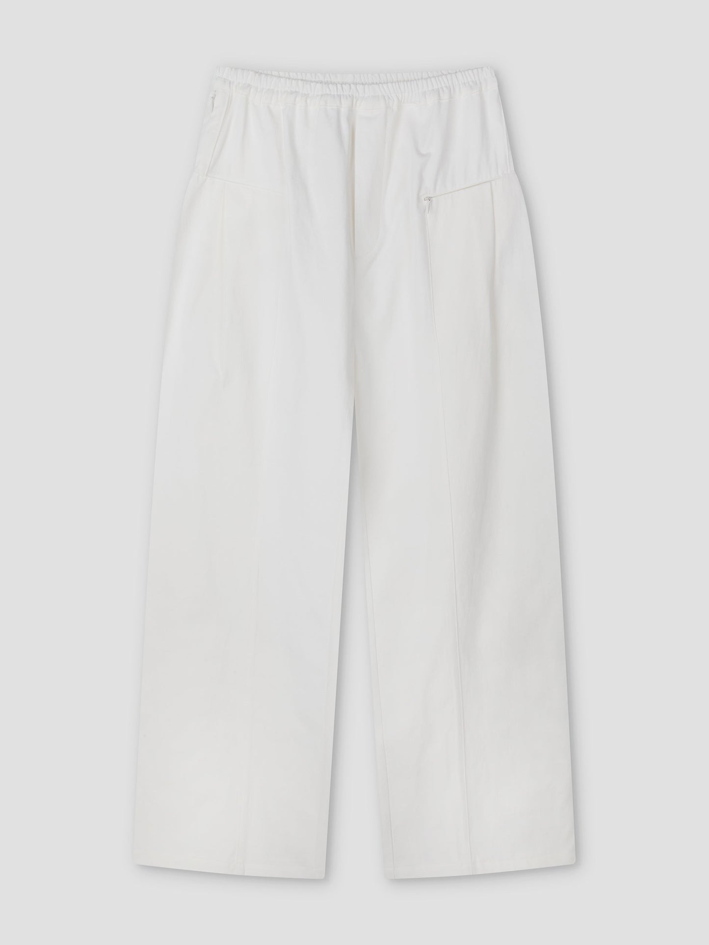The Pleat Pant - White features a relaxed straight-leg fit with an elasticated waistband, side pockets, a small zip pocket, and subtle front seam details, shown flat on a light grey background.