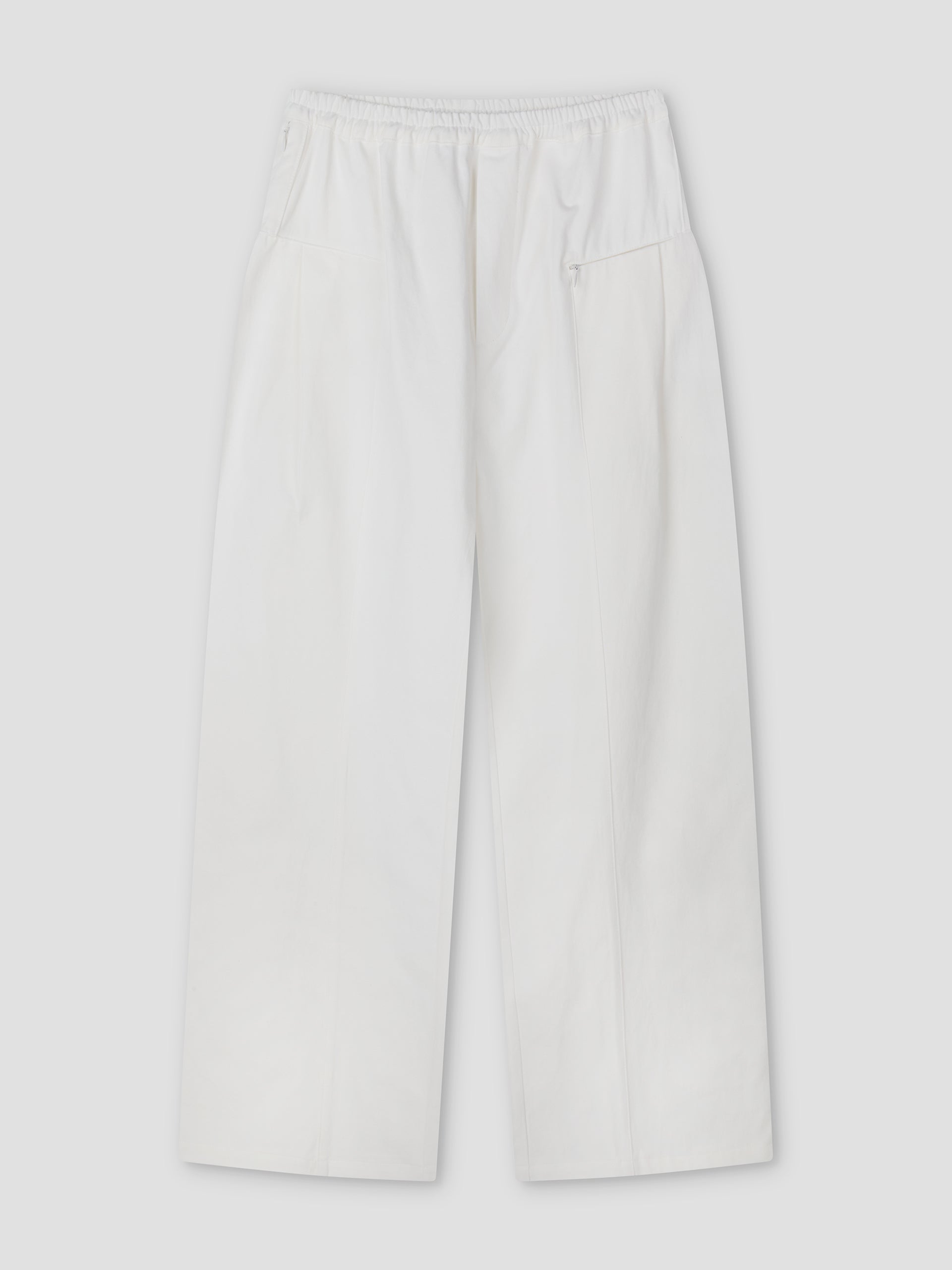 The Pleat Pant - White features a relaxed straight-leg fit with an elasticated waistband, side pockets, a small zip pocket, and subtle front seam details, shown flat on a light grey background.