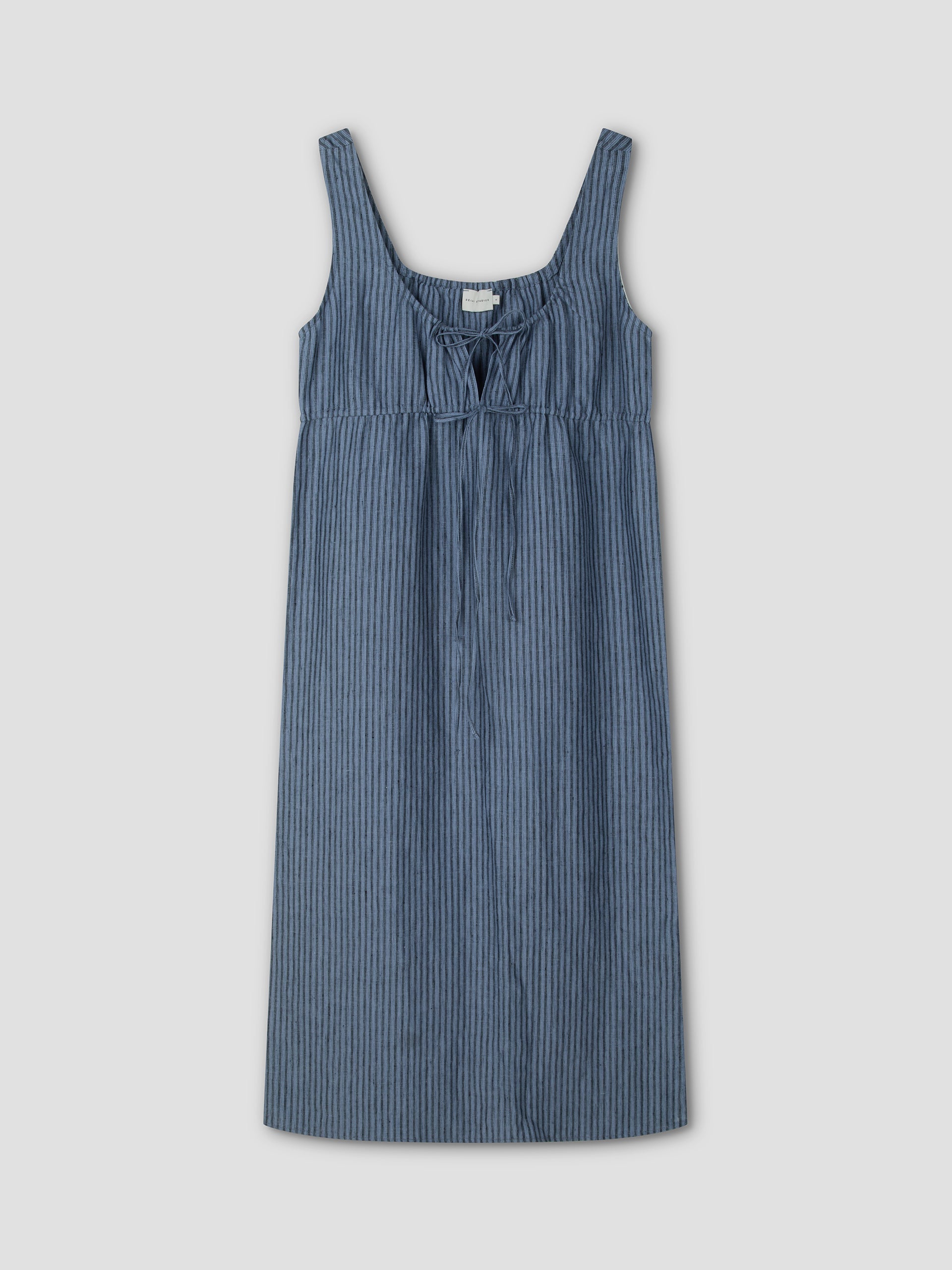 The Sleeveless Cord Dress - Azure Stripe by Deiji Studios features thin vertical white stripes, a scoop neckline, front tie detail, and a relaxed midi silhouette. Displayed on a plain light gray background.