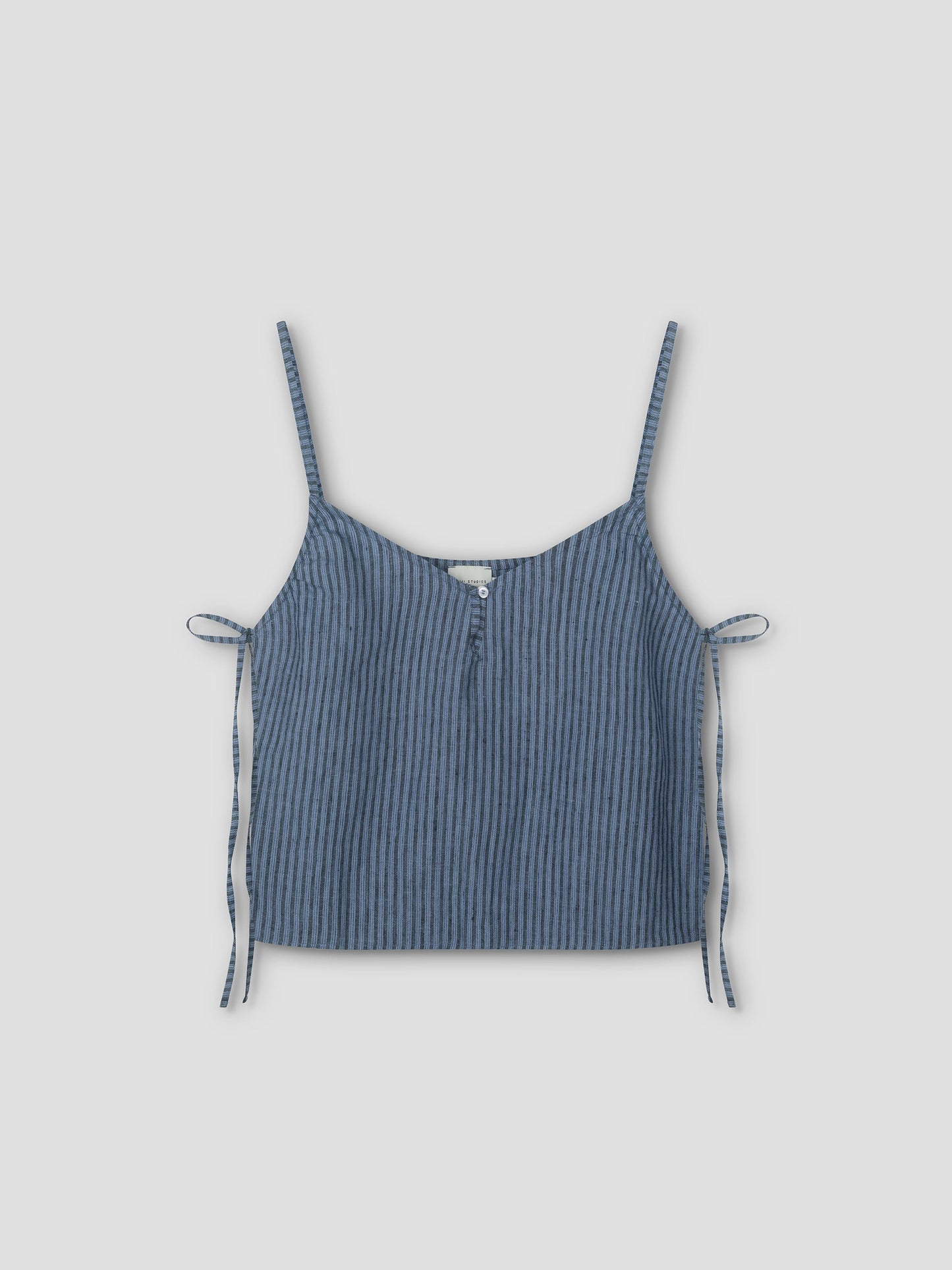 The V Neck Cami - Azure Stripe is a sleeveless crop top with thin shoulder straps, a front button, and side ties. Made from lightweight textured fabric for a relaxed feel, it features an azure stripe pattern on a light grey background.