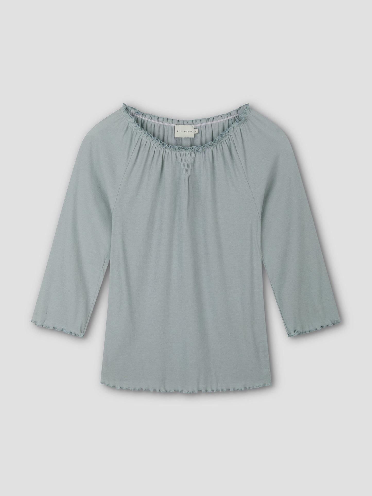 The Cotton Flounce 3/4 Sleeve - Baby Blue by Deiji Studios is a soft, fitted women's top with a scoop neck and ruffle details on the neckline and sleeves, shown against a plain white background.
