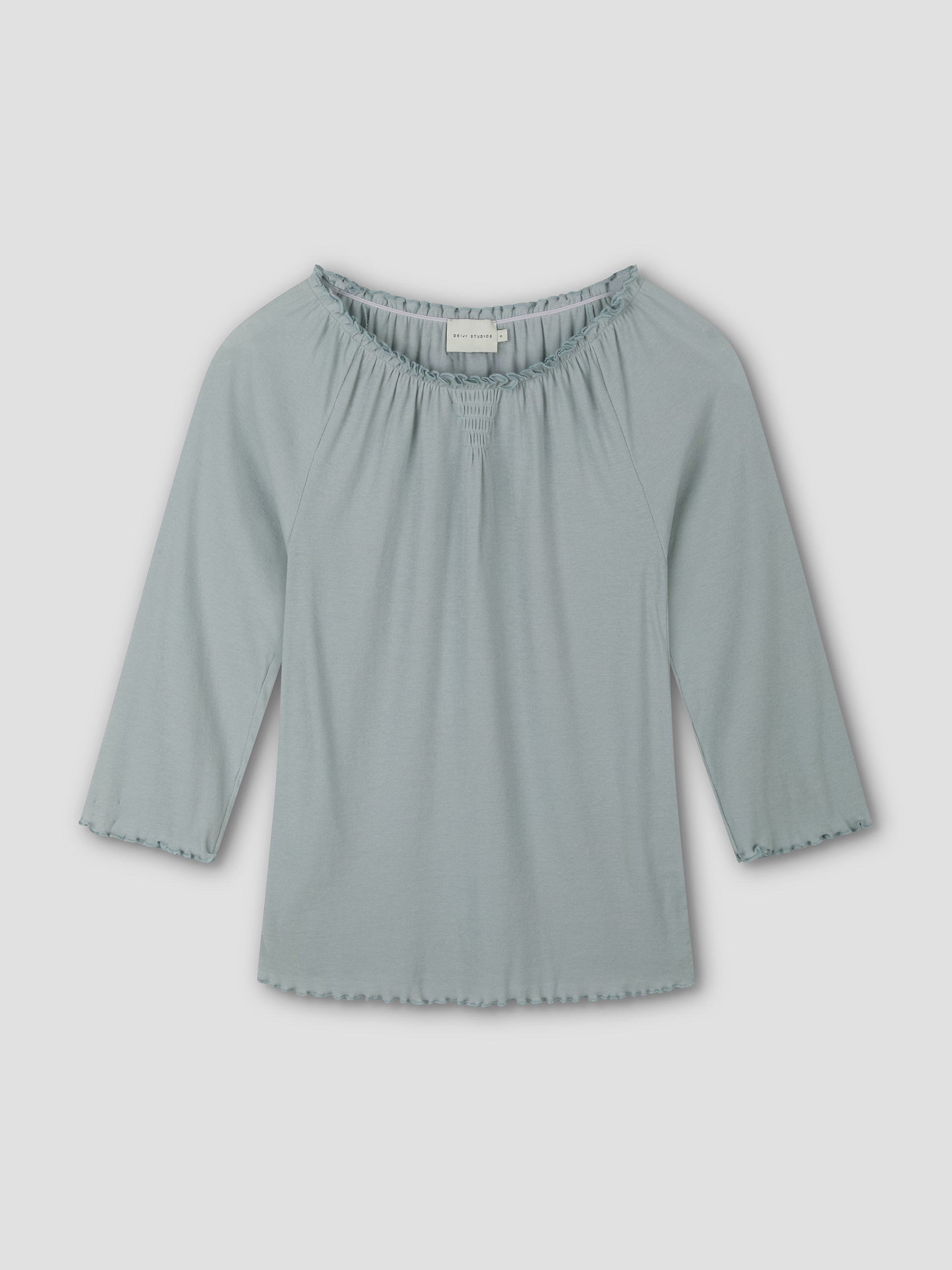 The Cotton Flounce 3/4 Sleeve - Baby Blue by Deiji Studios is a soft, fitted women's top with a scoop neck and ruffle details on the neckline and sleeves, shown against a plain white background.